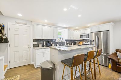 Kitchen with stainless steel appliances, a kitchen island, light hardwood / wood-style flooring, and white cabinetry | Image 3