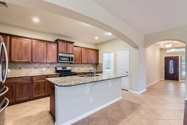 Kitchen featuring stainless steel appliances, tasteful backsplash, dark stone countertops, arched walkways, and a kitchen breakfast bar | Image 14