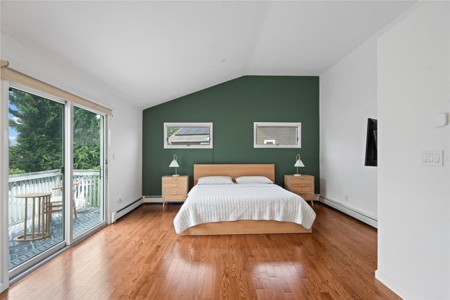 Bedroom with multiple windows, a baseboard radiator, access to exterior, vaulted ceiling, and wood finished floors | Image 23