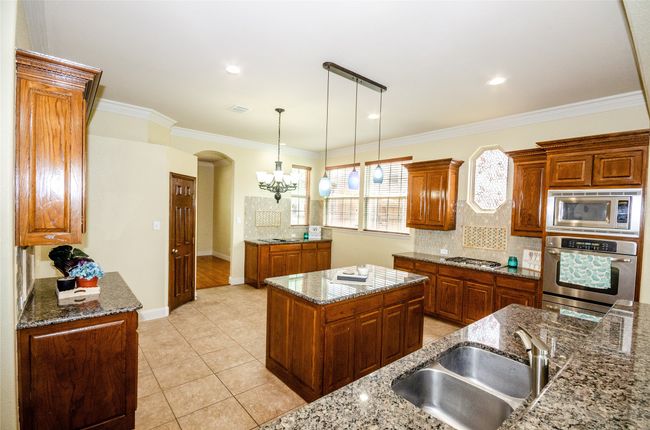 Kitchen featuring stainless steel appliances, a sink, decorative backsplash, pendant lighting, and crown molding | Image 5