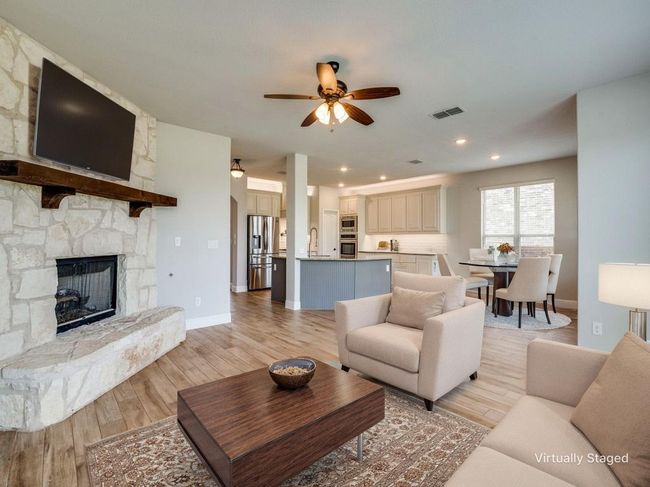 Living area featuring a ceiling fan, a stone fireplace, light wood finished floors, recessed lighting, and baseboards | Image 39