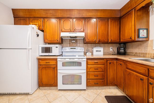 Kitchen with light tile patterned floors, brown cabinets, under cabinet range hood, and white appliances | Image 17