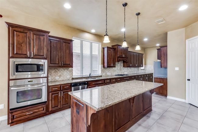 Kitchen featuring visible vents, a kitchen island, appliances with stainless steel finishes, a sink, and light stone counters | Image 13