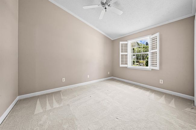 Empty room with ceiling fan, a textured ceiling, light colored carpet, crown molding, and baseboards | Image 11