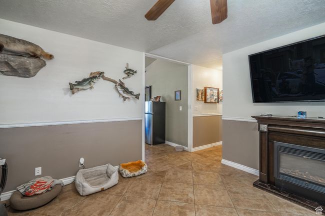 Living room with ceiling fan, a textured ceiling, light tile patterned floors, and a glass covered fireplace | Image 18