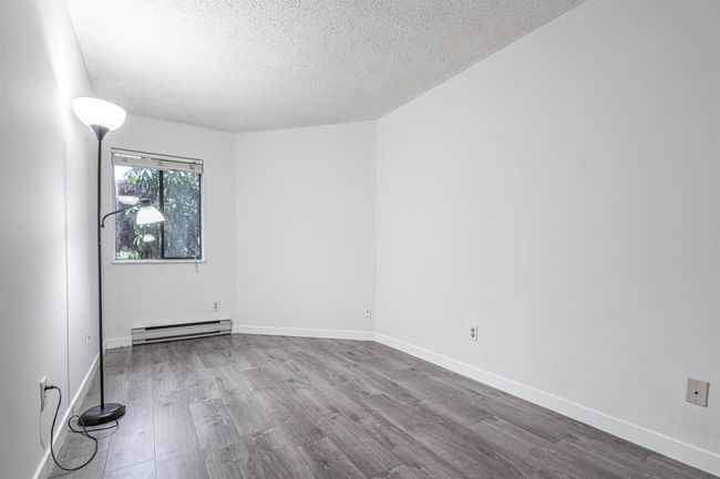 Empty room with baseboards, a baseboard heating unit, wood finished floors, and a textured ceiling | Image 12