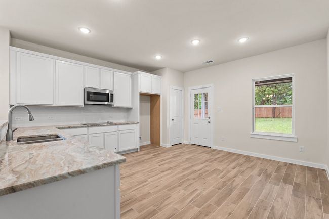 Kitchen with stainless steel microwave, a sink, light stone counters, white cabinetry, and recessed lighting | Image 12