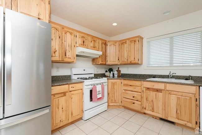 Kitchen with freestanding refrigerator, white gas stove, under cabinet range hood, light brown cabinets, and dark countertops | Image 39