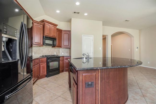 Take a closer look at the heart of this kitchen—featuring a striking curved island that adds both style and function. The dark granite countertops contrast beautifully with the warm wood cabinets, while the built-in appliances and tile backsplash give it a timeless, classic feel. | Image 12