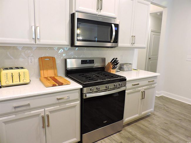 Kitchen featuring appliances with stainless steel finishes, light countertops, white cabinets, light wood-style flooring, and backsplash | Image 6