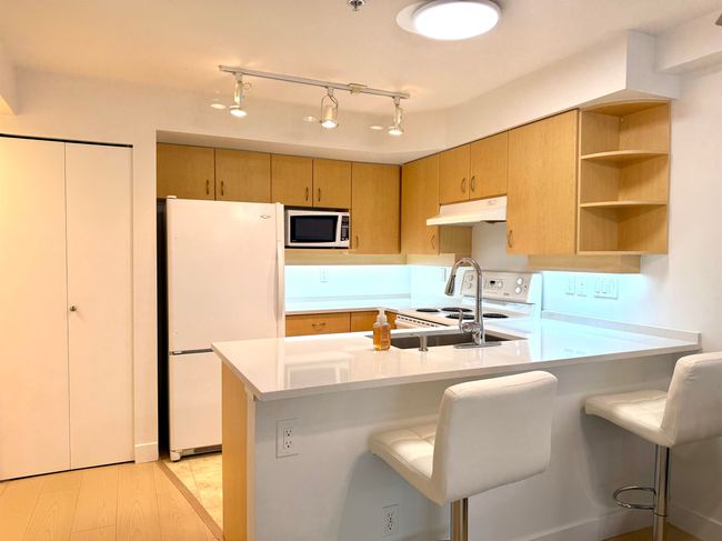 Kitchen with white appliances, under cabinet range hood, light countertops, and a peninsula | Image 8