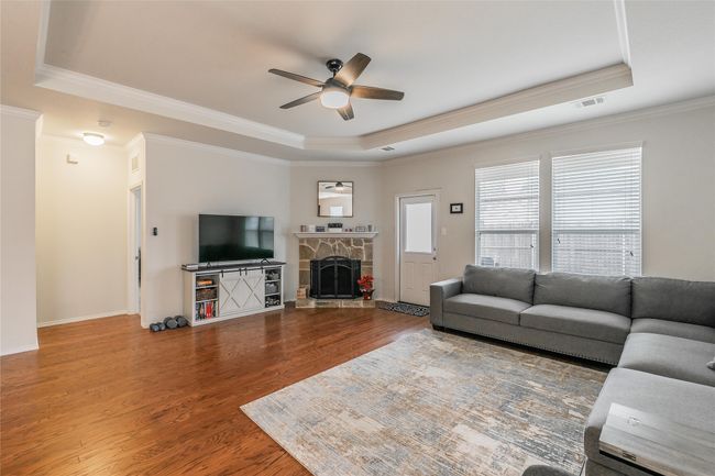 Living room featuring wood-type flooring, a tray ceiling, ceiling fan, a fireplace, and ornamental molding | Image 23