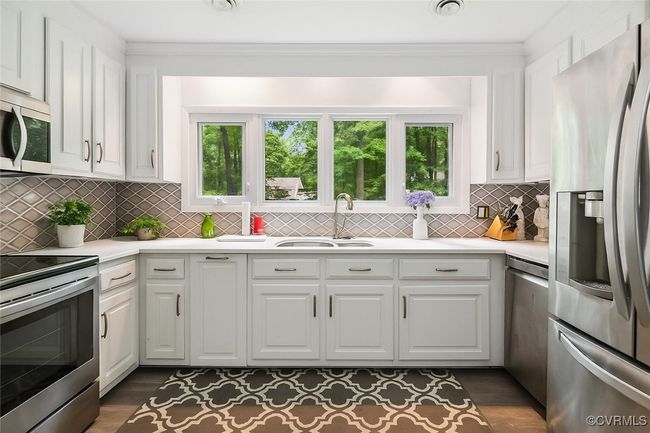 Kitchen with stainless steel appliances, white cabinetry, light countertops, tasteful backsplash, and ornamental molding | Image 6