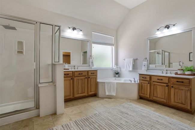 Bathroom with vaulted ceiling, a stall shower, two vanities, a garden tub, and tile patterned floors | Image 19