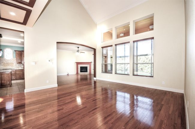 Unfurnished living room with a ceiling fan, wood finished floors, high vaulted ceiling, a fireplace, and arched walkways | Image 8