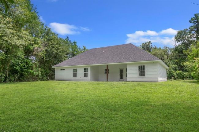 This photo showcases a single-story, white house with a sloped roof, set on a spacious, grassy lot surrounded by trees, offering a serene and private setting. | Image 21