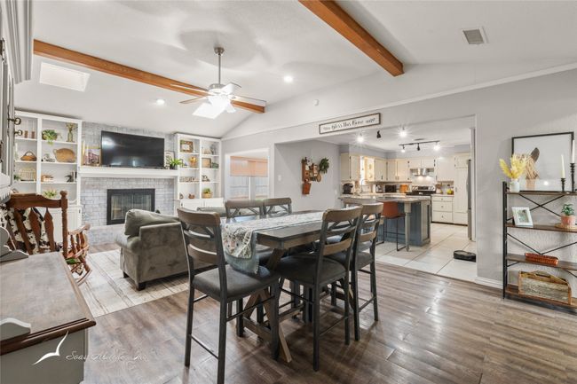 Dining room featuring ceiling fan, lofted ceiling with beams, light wood-style floors, a brick fireplace, and visible vents | Image 6