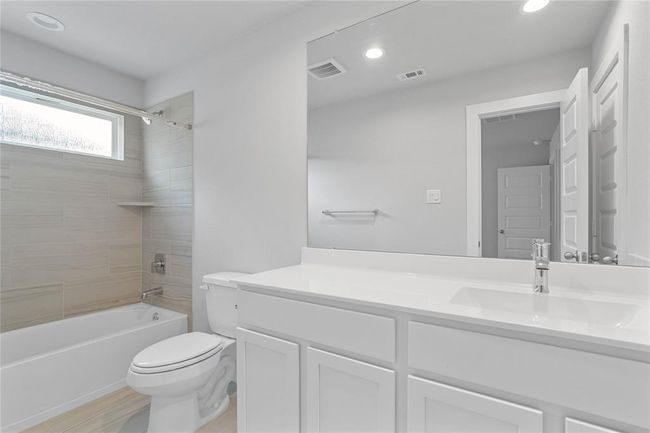 Secondary bath features tile flooring, bath/shower combo with tile surround, stained cabinets, beautiful light countertops, mirror, sleek fixtures and modern finishes. | Image 19