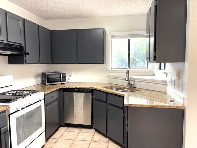 Kitchen featuring stainless steel appliances, under cabinet range hood, a textured ceiling, and light tile patterned floors | Image 6
