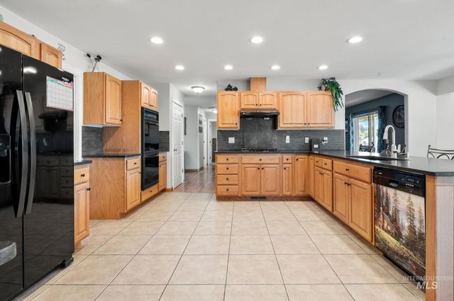 Kitchen with including double oven & gas cooktop, refrigerator, dishwasher &honed black granite countertops, decorative backsplash, under cabinet range hood, and recessed lighting | Image 10