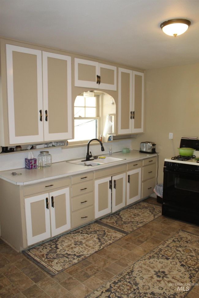 Kitchen featuring black gas stove, stone finish flooring, white cabinets, light countertops, and arched walkways | Image 4