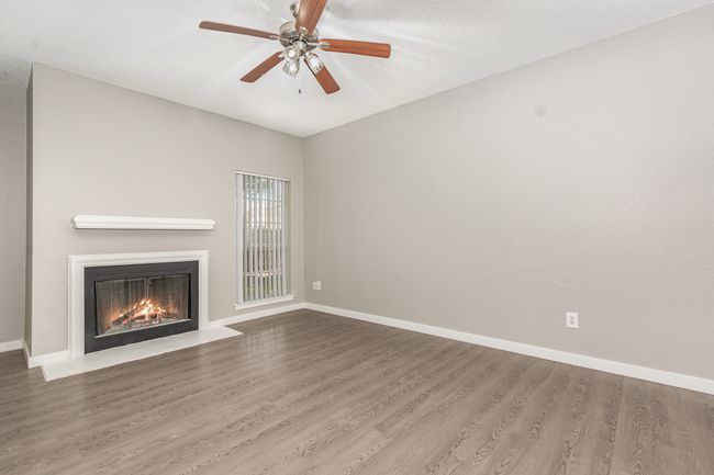 Unfurnished living room featuring a fireplace with flush hearth, wood finished floors, baseboards, ceiling fan, and a textured ceiling | Image 6