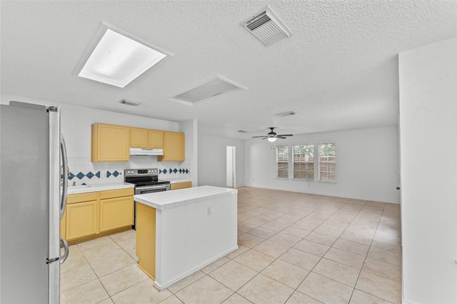 Kitchen featuring appliances with stainless steel finishes, under cabinet range hood, a kitchen island, tile countertops, and light tile patterned floors | Image 15