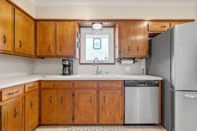 Kitchen featuring stainless steel appliances, brown cabinetry, light countertops, and crown molding | Image 12