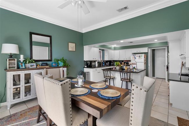 This open-concept dining and kitchen area offers a welcoming and functional space for entertaining. The dining area features a rich wooden table with seating for six, while the adjacent kitchen boasts a spacious island with additional bar seating. White cabinetry, granite countertops, and recessed lighting enhance the kitchen’s modern appeal, while the green accent walls and crown molding add warmth and character. | Image 21
