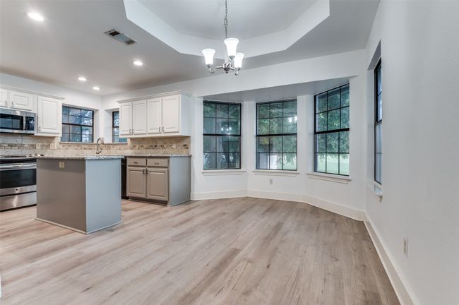 Kitchen with stainless steel appliances, light wood finished floors, decorative backsplash, a chandelier, and white cabinets | Image 7