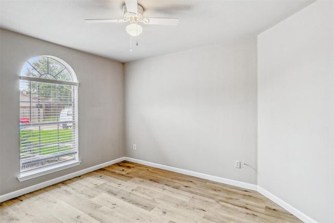 This home also includes two secondary bedrooms, each featuring vinyl flooring, decorator paint, and ceiling fans for added comfort. This particular room is highlighted by a beautiful arched window with a view of the front yard. | Image 25