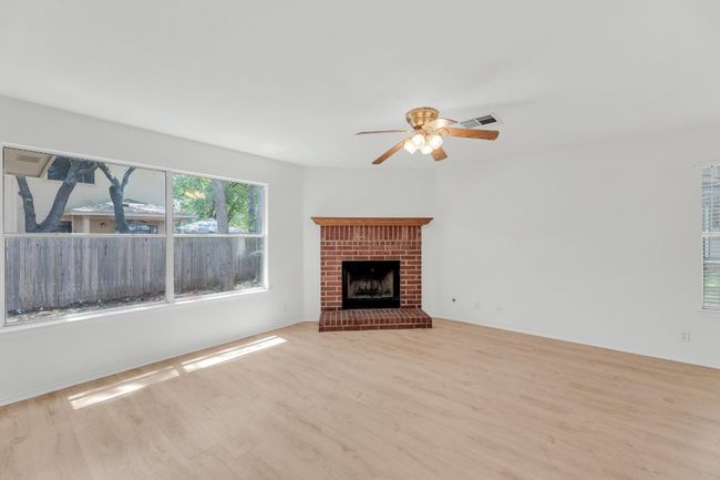 Unfurnished living room featuring wood finished floors, visible vents, a ceiling fan, and a brick fireplace | Image 4