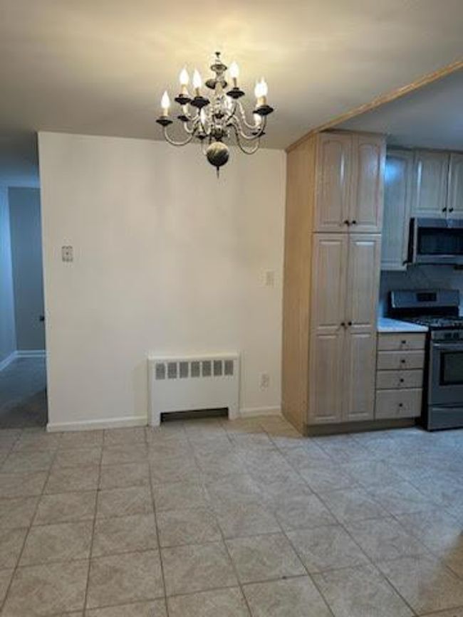 Kitchen featuring radiator heating unit, stainless steel appliances, an inviting chandelier, light tile patterned floors, and baseboards | Image 6