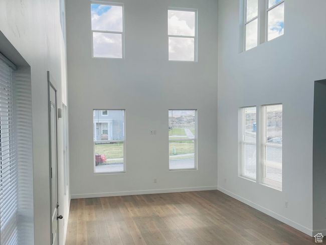 Unfurnished living room featuring a towering ceiling, baseboards, a wealth of natural light, and light wood-style floors | Image 6