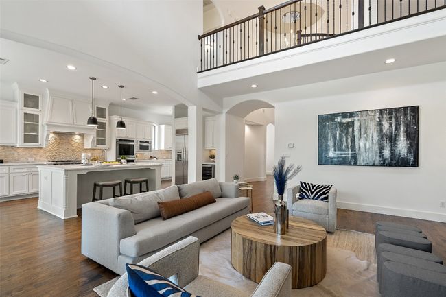 Living room with arched walkways, dark wood-style floors, a towering ceiling, recessed lighting, and wine cooler | Image 15