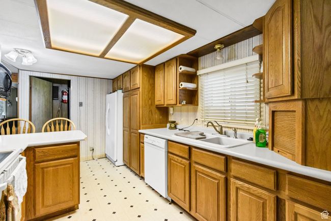 Kitchen with white appliances, a sink, light floors, open shelves, and brown cabinets | Image 11