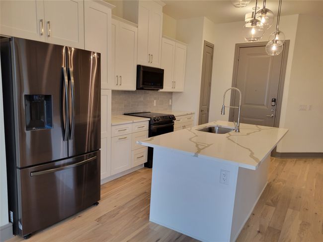 Kitchen with stainless steel fridge with ice dispenser, a kitchen island with sink, black range with electric stovetop, backsplash, and white cabinetry | Image 9