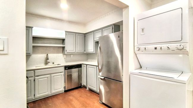 Kitchen with sink, stacked washing maching and dryer, appliances with stainless steel finishes, tasteful backsplash, and wood-type flooring | Image 10
