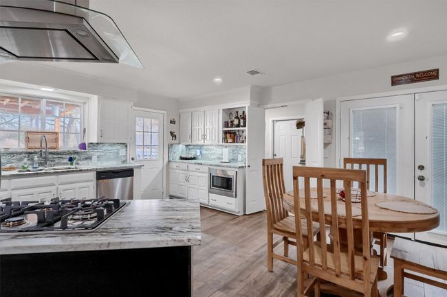 Kitchen with white cabinetry, range hood, light stone countertops, backsplash, and light wood finished floors | Image 13