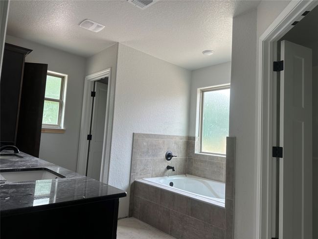 Full bathroom featuring double vanity, a garden tub, a sink, a textured ceiling, and a textured wall | Image 12