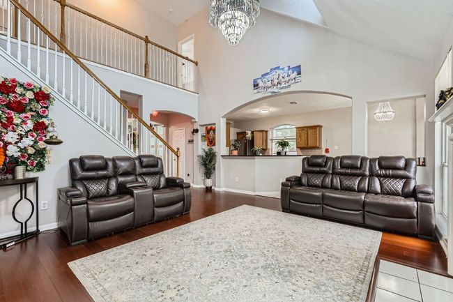 Living room with arched walkways, high vaulted ceiling, dark wood-style flooring, and a chandelier | Image 6