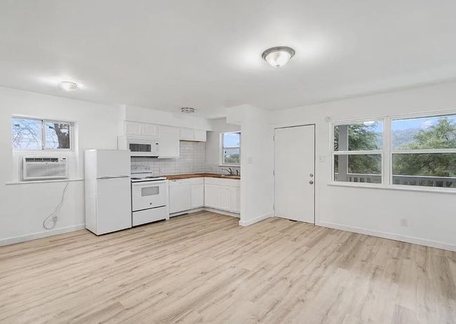 Kitchen with white appliances, cooling unit, light wood finished floors, white cabinets, and backsplash | Image 12