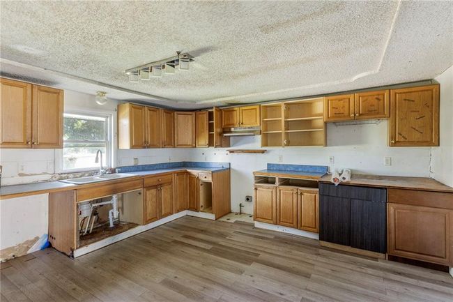Kitchen with under cabinet range hood, light wood finished floors, a textured ceiling, open shelves, and brown cabinets | Image 11