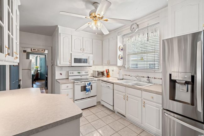 Kitchen featuring white appliances, white cabinetry, backsplash, light tile patterned floors, and a ceiling fan | Image 7