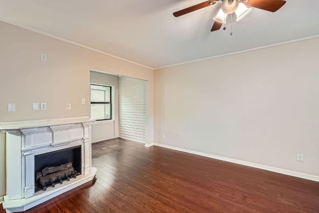 Unfurnished living room with a ceiling fan, a fireplace with raised hearth, baseboards, ornamental molding, and dark wood-style flooring | Image 6