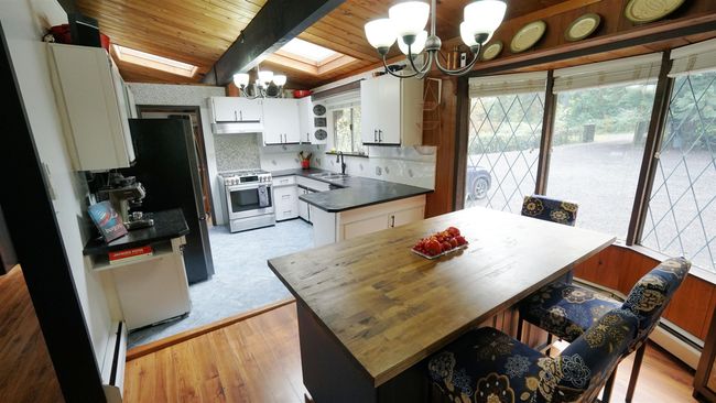 Kitchen with a chandelier, a kitchen island, white cabinetry, appliances with stainless steel finishes, and dark countertops | Image 6