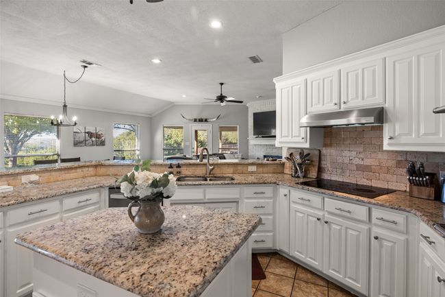 Kitchen featuring black electric cooktop, lofted ceiling, under cabinet range hood, visible vents, and a sink | Image 4