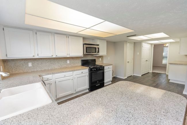 Kitchen with light countertops, gas stove, a sink, stainless steel microwave, and dark wood-style flooring | Image 8