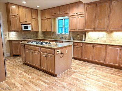 Kitchen with a kitchen island with sink, light stone countertops, light wood-type flooring, white appliances, and tasteful backsplash | Image 2