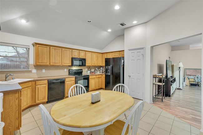 Kitchen featuring black appliances, vaulted ceiling, tasteful backsplash, light tile patterned floors, and light countertops | Image 13